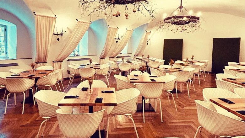 Eleganter Speisesaal mit Parkettboden, weißen Stühlen, Holztischen und dekorativen Kronleuchtern.