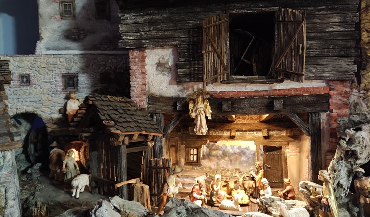 Detailreiche Krippe mit Figuren in einer rustikalen Scheune, umgeben von Schafen und Hirten.