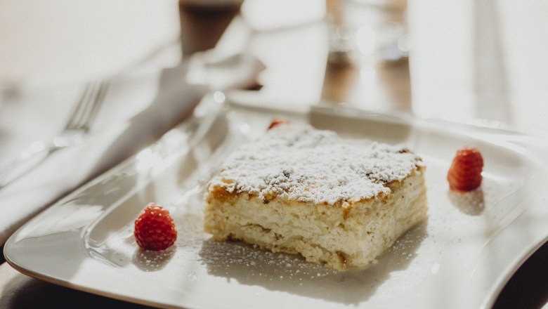 Ein Stück Milchrahmstrudel mit Puderzucker und Himbeeren auf einem weißen Teller.