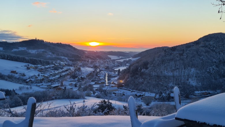 Winterlandschaft mit Sonnenaufgang über einem verschneiten Dorf in einem Tal.