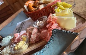 Eine rustikale Jause mit Wurst, Käse, Brot und Aufstrichen auf einem Holzteller.