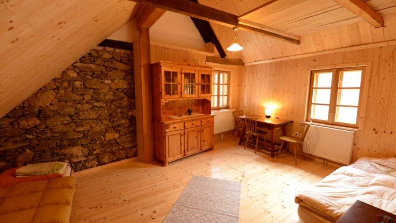 Gem&uuml;tliches Zimmer mit Holzw&auml;nden, zwei Betten, Tisch und St&uuml;hlen, Schrank und Steinwand.