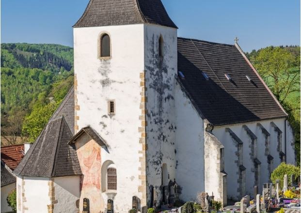Rustikale Wehrkirche Bromberg mit breitem Turm und Friedhof im Vordergrund.