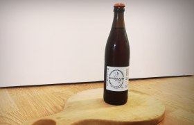 Eine Flasche Weizenbier vom Holzbr&auml;u steht auf einem runden Holzbrett mit Griff.