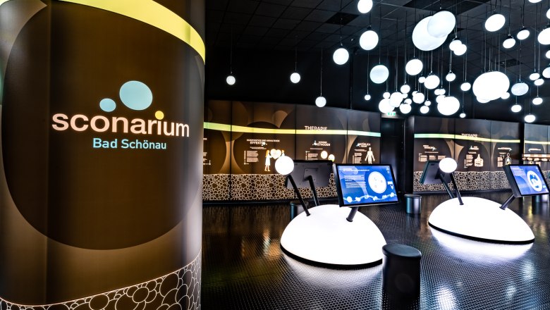Innenansicht der Ausstellung Sconarium in Bad Sch&ouml;nau mit interaktiven Displays und leuchtenden Kugeln an der Decke.