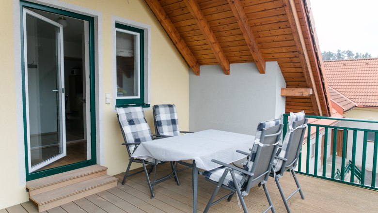 Dachterrasse mit Tisch und St&uuml;hlen unter einem Holzdach.