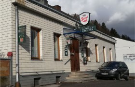 Außenansicht des traditionellen Gasthauses Brunner mit geschindelter, weißer Fassade und Stiegl Schild