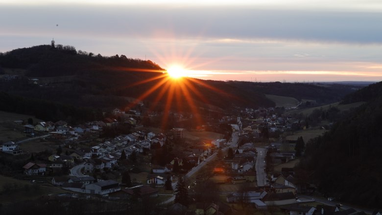 Sonnenaufgang hinter einem H&uuml;gel mit einem Dorf im Vordergrund.