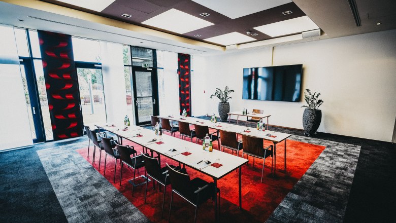 Moderner Seminarraum mit Tischen, Stühlen und großem Bildschirm.