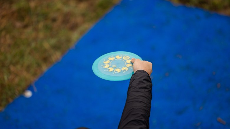 Person h&auml;lt eine Discgolf-Scheibe &uuml;ber einer blauen Matte, die Hand zum Wurf ausgestreckt