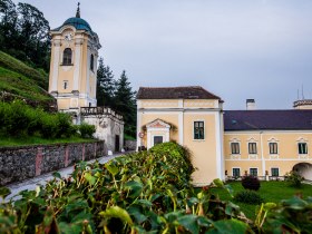 Schloss mit Turm in Bad Erlach, eine Stra&szlig;e f&uuml;hrt durch, umgeben von gr&uuml;ner Landschaft.