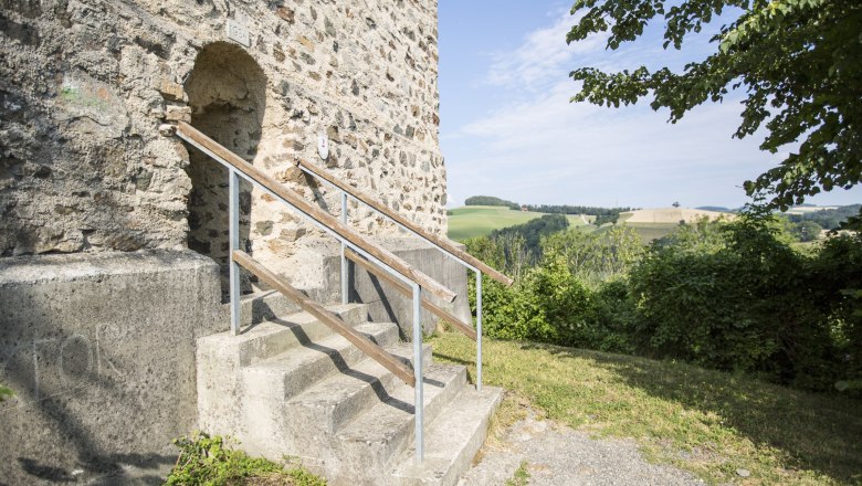 Eingang zum Feuerturm der Burgruine Kirchschlag mit Treppe und Landschaft im Hintergrund.