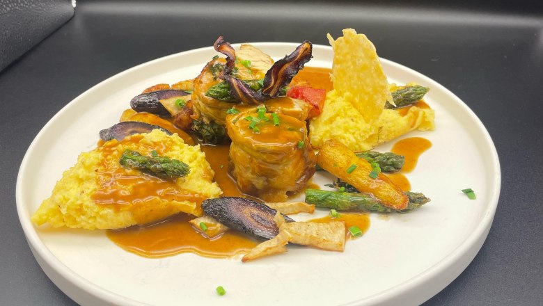 Gourmetgericht auf weißem Teller mit Fleisch, Gemüse und Sauce.