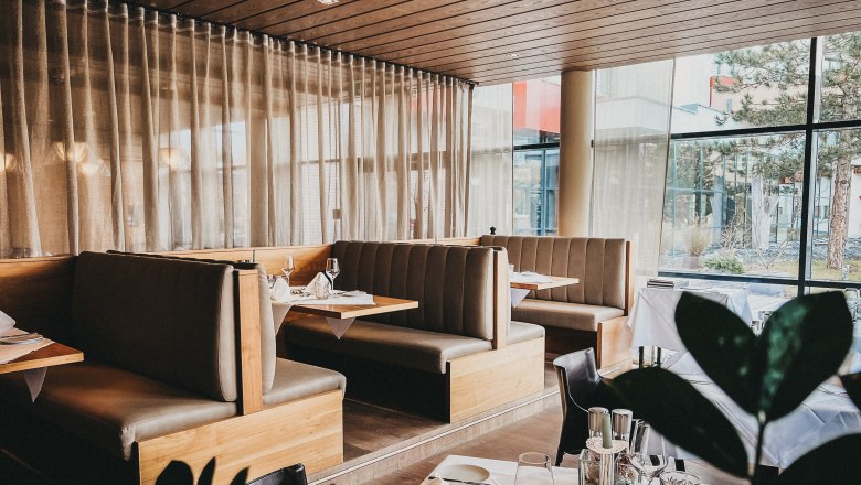 Innenansicht eines eleganten Restaurants mit Holzmöbeln und großen Fenstern.