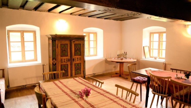 Gem&uuml;tliche Stube mit Holzm&ouml;beln, Tischdecken und einem bemalten Schrank.