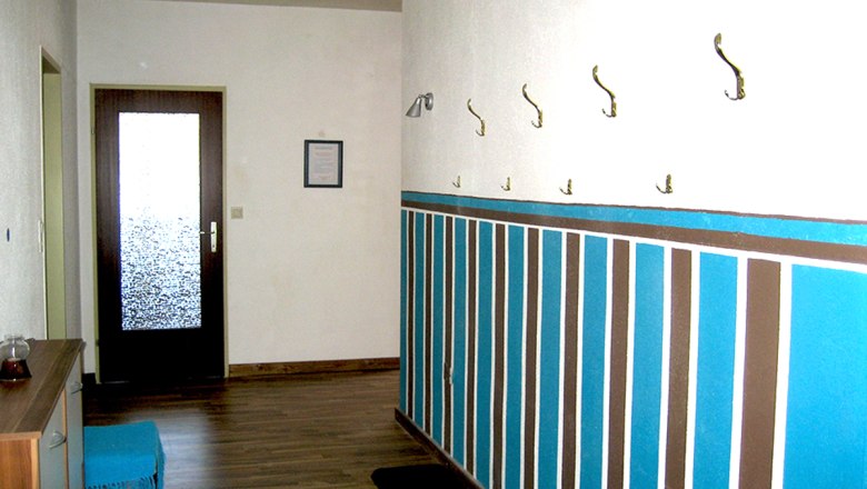 Flur mit Holzboden, bunter Wandgestaltung und Garderobenhaken.