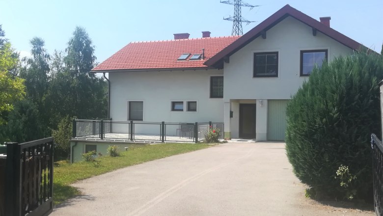 Zweistöckiges Haus mit rotem Dach und Garage, umgeben von Bäumen und Sträuchern.