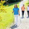 Drei Personen beim Nordic Walking auf einem Kiesweg in einem grünen Park. Eine der Personen ist eine Trainerin des Gesundheitsresorts Königsberg.
