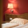 Ein gemütliches Doppelzimmer mit Holzkopfteil, roter Wand und Wandlampe.