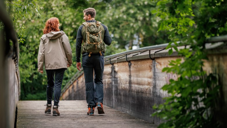 Zwei Wandernde auf einer Holzbrücke im Wald