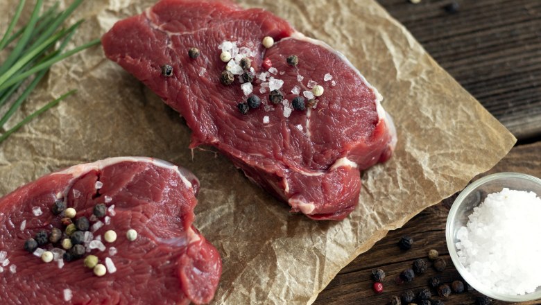 Zwei Stück rohes Rindfleisch mit Salz und Pfeffer bestreut auf Backpapier, daneben Schnittlauch, eine Schale Salz und Pfeffer.