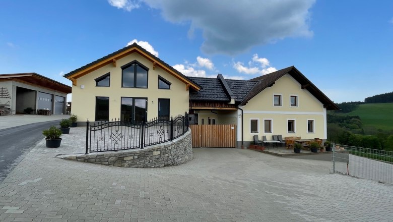 Gelbes Haus mit großen Fenstern auf gepflasterter Fläche unter blauen Himmel.