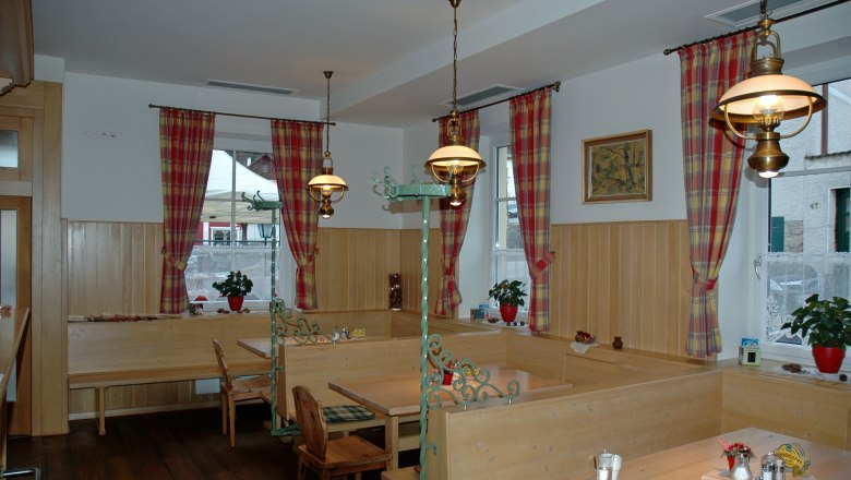 Gemütlicher Gastraum mit Holzmöbeln und karierten Vorhängen.