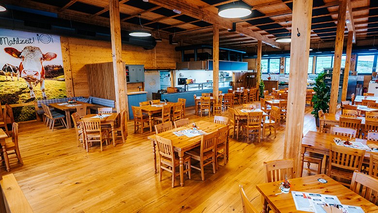 Rustikales Restaurant mit Holzeinrichtung, eckigen Tischen und Stühlen sowie Säulen.