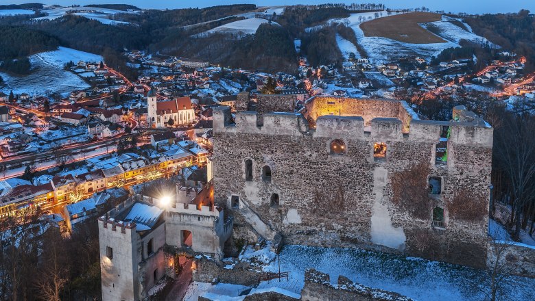 Burgruine Kirchschlag bei D&auml;mmerung mit beleuchteter Stadt im Hintergrund.