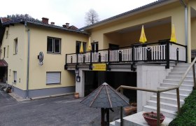 Gelbes Gasthaus mit Terrasse und Treppe.