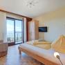 Helles Schlafzimmer mit Bett, Sofa, Schrank und Balkon mit Aussicht.