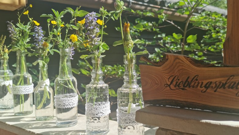 Kleine Glasflaschen mit Wiesenblumen und ein Holzschild mit der Aufschrift 'Lieblingsplatz'.