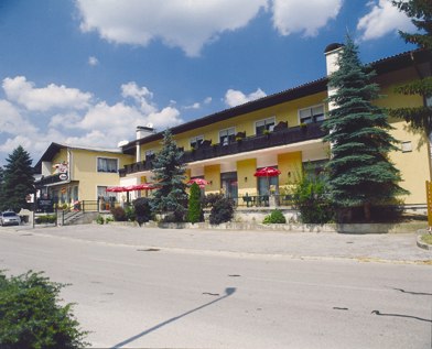 Gelbes Geb&auml;ude mit Caf&eacute; und Restaurant, umgeben von B&auml;umen, unter blauem Himmel.