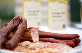 Nahaufnahme von Wurst- und Fleischspezialit&auml;ten auf einem Teller mit Flaschen im Hintergrund.