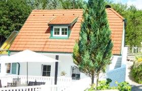 Au&szlig;enansicht eines wei&szlig;en Ferienhauses mit rotem Dach und Terrasse.