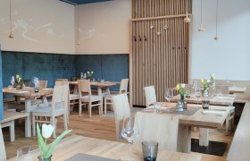 Modernes Restaurant mit Holzmöbeln, gedeckten Tischen, Deckenlampen und blauen Akzenten.