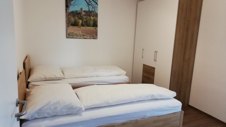 Ein Schlafzimmer mit zwei Einzelbetten, einem Kleiderschrank und einem Landschaftsbild an der Wand.