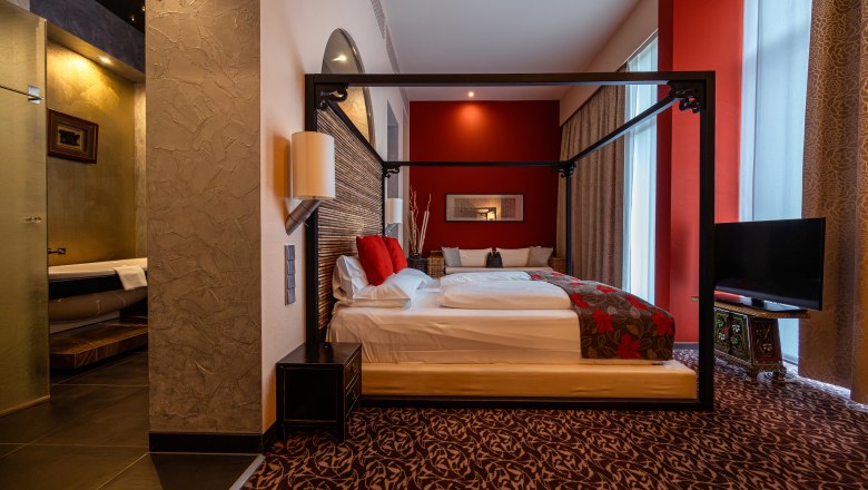 Hotelzimmer mit Himmelbett, roten Akzenten und asiatischem Dekor.