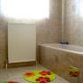 Ein Badezimmer mit beiger Fliesenwand, Badewanne, Heizkörper und bunten Teppichen.