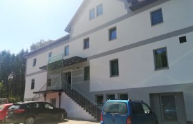 Au&szlig;enansicht eines modernen Gasthauses mit mehreren Fenstern und parkenden Autos davor.