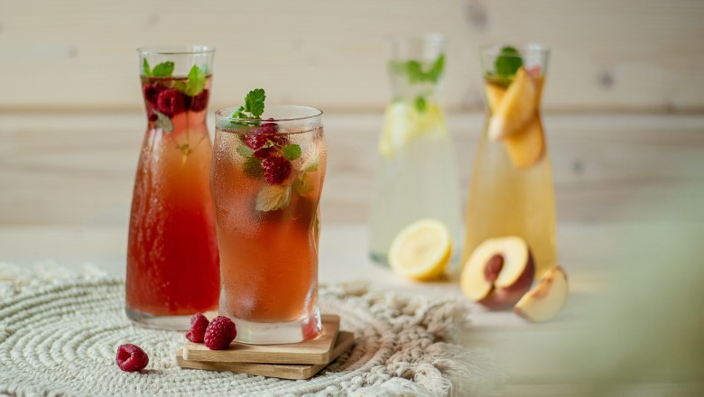 Verschiedene Gläser mit Limonade, dekoriert mit Früchten und Minze, auf einem Tisch.