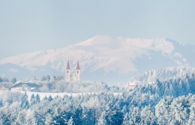 Winterlandschaft mit Kirche und Bergen im Hintergrund.