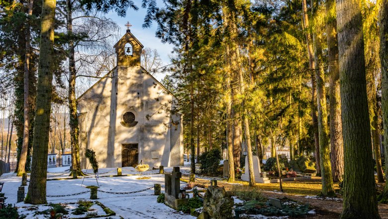 Winterliche Kapelle im Wald mit schneebedecktem Boden und Gr&auml;bern.