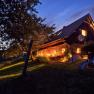 Ein beleuchtetes Ferienhaus bei Nacht mit Garten und Liegestuhl.