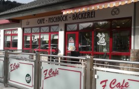 Au&szlig;enansicht eines Caf&eacute;s mit rotem Rahmen und Beschriftung 'Caf&eacute; Fischb&ouml;ck B&auml;ckerei'.