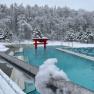 Ein verschneites Au&szlig;enbecken einer Therme mit roten asiatischen Elementen und schneebedeckten B&auml;umen im Hintergrund.