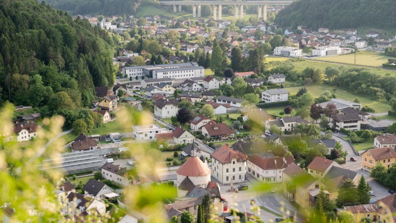 Blick auf Scheiblingkirchen mit Rundkirche und umliegenden H&auml;usern, im Hintergrund eine Autobahnbr&uuml;cke und bewaldete H&uuml;gel.